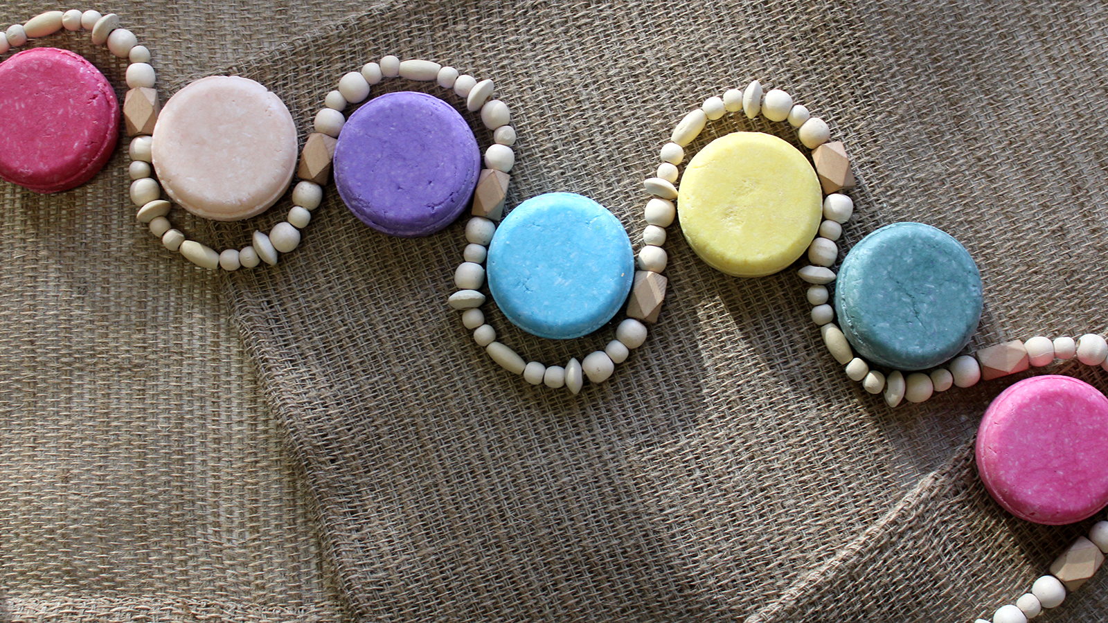 Flat lay of round multicolored shampoo bar with a string of wooden beads snaking around the bars, on a background of burlap. Alpaca Soaps AlpacaSoaps