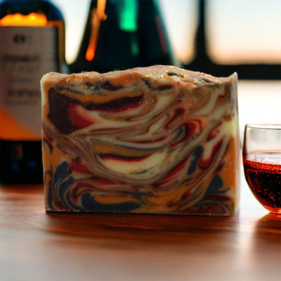 Bourbon Street Bar Soap on a wooden bar with bottles and a glass of bourbon in the foreground and background, Alpaca Soaps AlpacaSoaps